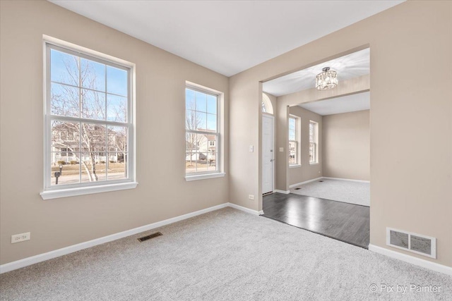 carpeted entrance foyer featuring a notable chandelier, visible vents, and baseboards