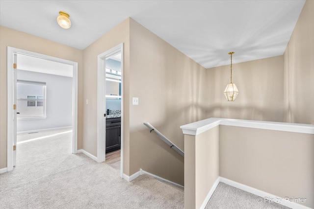 corridor featuring baseboards, an upstairs landing, and carpet floors