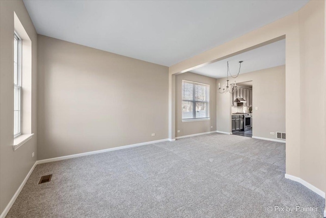 unfurnished living room with an inviting chandelier, carpet flooring, baseboards, and visible vents