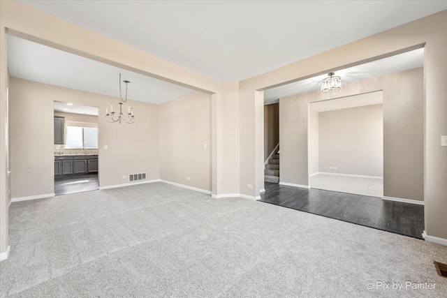 unfurnished living room featuring carpet, baseboards, visible vents, stairs, and a chandelier