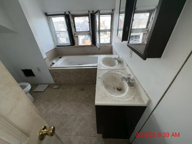 full bathroom with tile patterned flooring, tiled bath, toilet, double vanity, and a sink