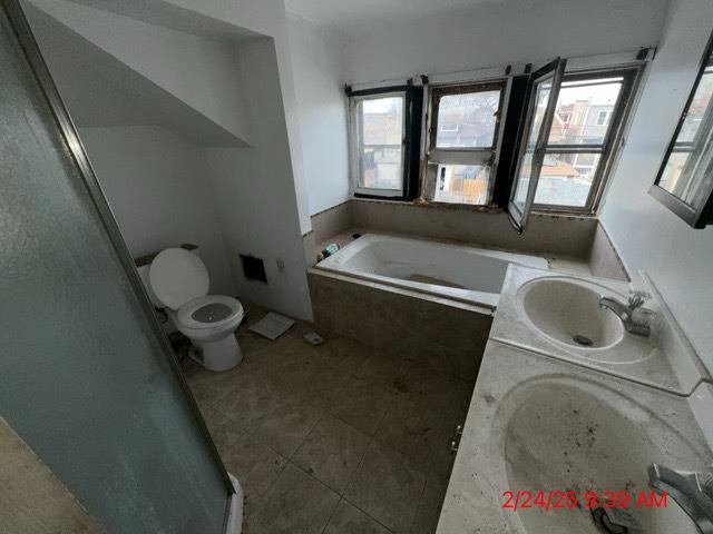 bathroom featuring toilet, a garden tub, and a sink