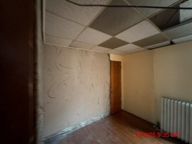 basement featuring radiator, a paneled ceiling, and wood finished floors