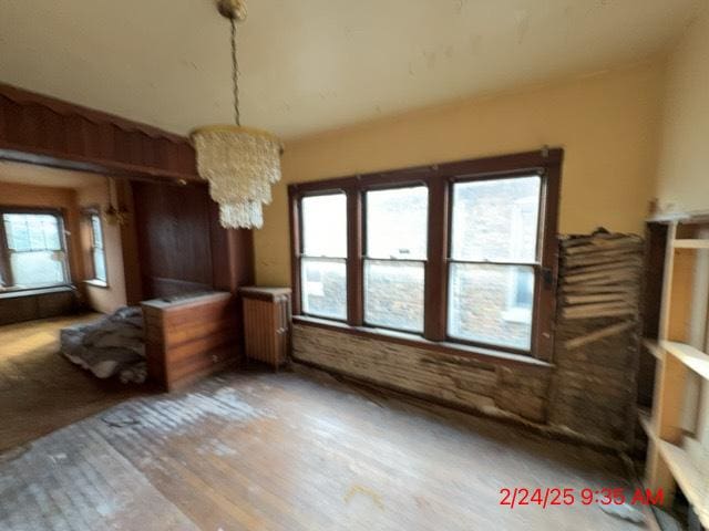 unfurnished dining area with an inviting chandelier, radiator, and wood finished floors