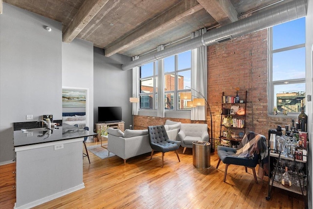 living area with brick wall, light wood-type flooring, and a towering ceiling