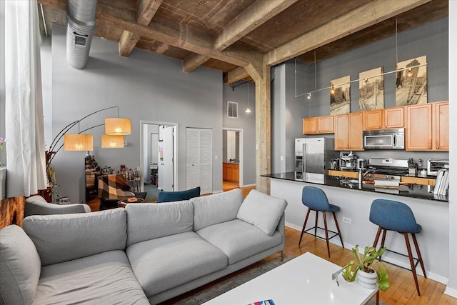 living room with light wood finished floors, visible vents, baseboards, a toaster, and a towering ceiling