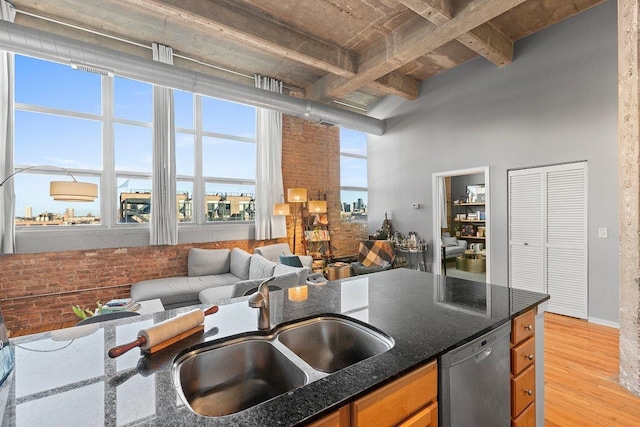 kitchen with light wood-type flooring, a sink, brick wall, dishwasher, and a towering ceiling