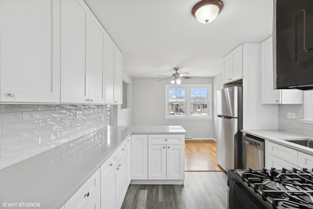 kitchen featuring wood finished floors, stainless steel appliances, white cabinets, light countertops, and decorative backsplash