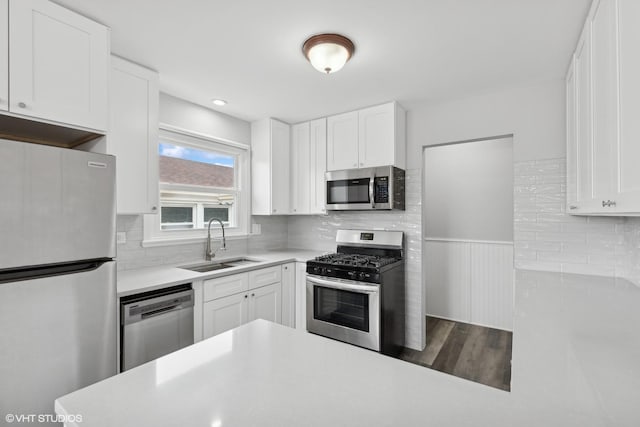 kitchen with a sink, light countertops, white cabinets, appliances with stainless steel finishes, and wainscoting