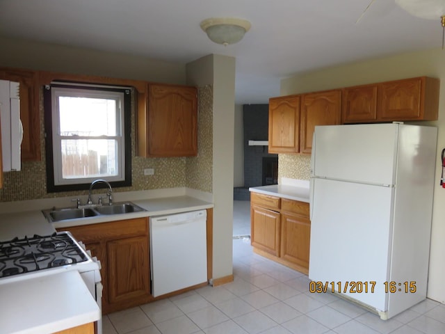 kitchen with a sink, tasteful backsplash, white appliances, brown cabinetry, and light countertops