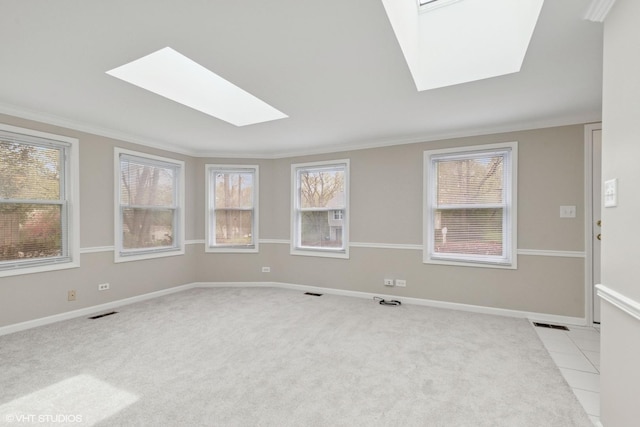 unfurnished room with a skylight, ornamental molding, light carpet, baseboards, and light tile patterned floors