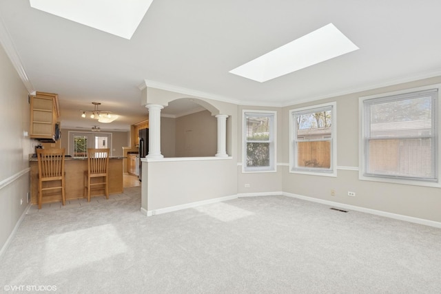 unfurnished living room featuring a skylight, ornamental molding, healthy amount of natural light, light colored carpet, and ornate columns