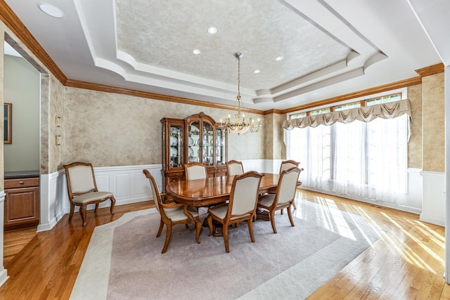 dining room featuring a tray ceiling, light wood-style floors, a chandelier, and wainscoting