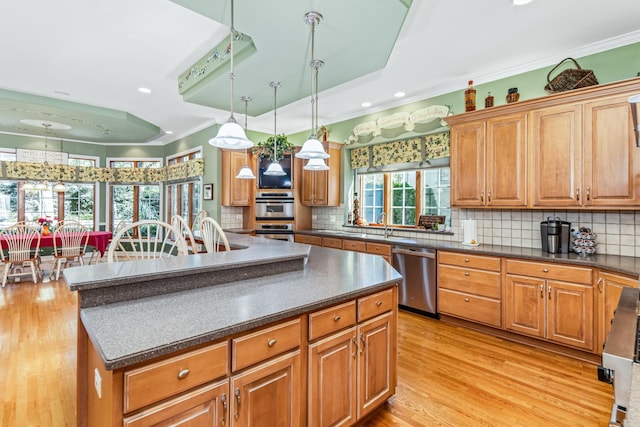 kitchen with dark countertops, light wood-style flooring, ornamental molding, appliances with stainless steel finishes, and a raised ceiling