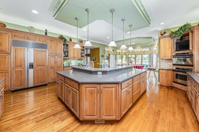 kitchen featuring dark countertops, double oven, ornamental molding, brown cabinets, and paneled refrigerator