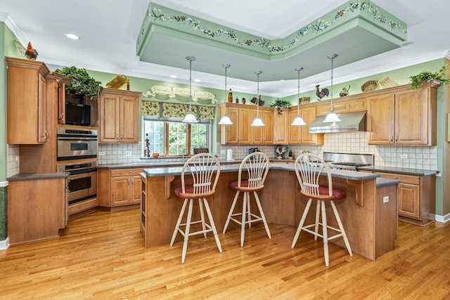 kitchen featuring a tray ceiling, light wood-style flooring, brown cabinetry, and under cabinet range hood