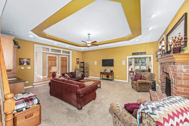 carpeted living area with a raised ceiling, a ceiling fan, recessed lighting, a fireplace, and baseboards