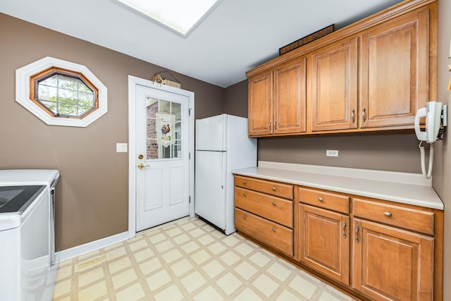 kitchen with washer and dryer, freestanding refrigerator, brown cabinetry, light countertops, and light floors