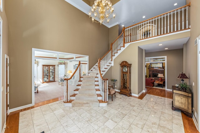 foyer entrance with baseboards, an inviting chandelier, a high ceiling, a fireplace, and stairs