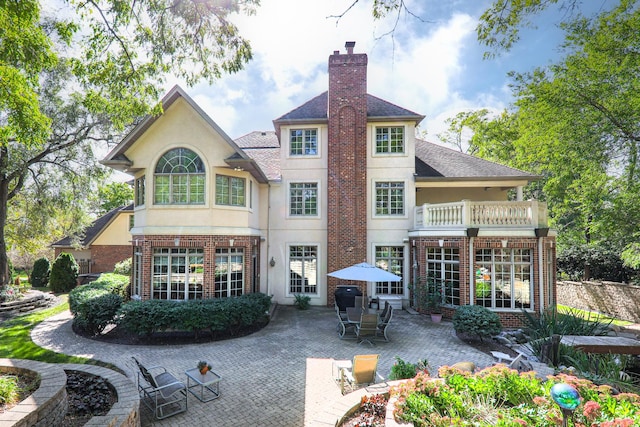 rear view of house featuring stucco siding, a balcony, brick siding, a chimney, and a patio area