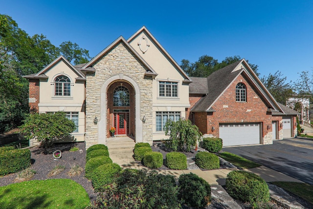 view of front facade with driveway, an attached garage, a shingled roof, stucco siding, and brick siding