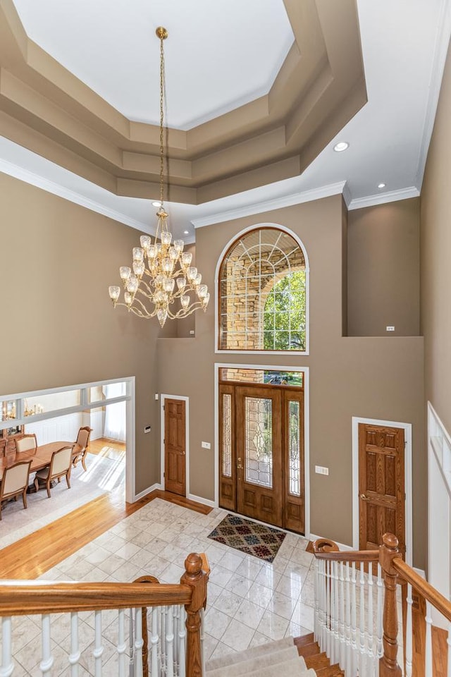 entrance foyer with a tray ceiling, a high ceiling, a notable chandelier, and baseboards