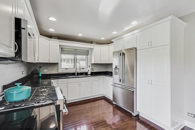 kitchen with a sink, dark countertops, dark wood-style floors, stainless steel appliances, and white cabinets