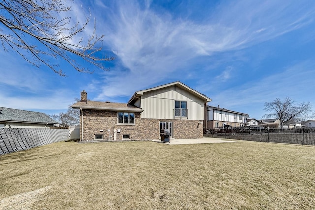 back of property with brick siding, a chimney, a fenced backyard, a yard, and a patio area