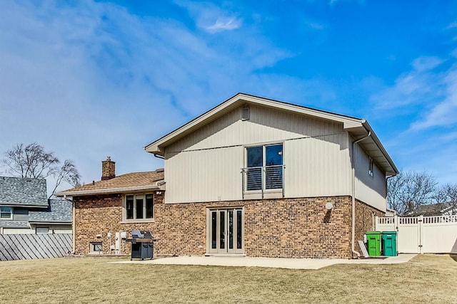 back of property featuring brick siding, fence private yard, french doors, a chimney, and a yard