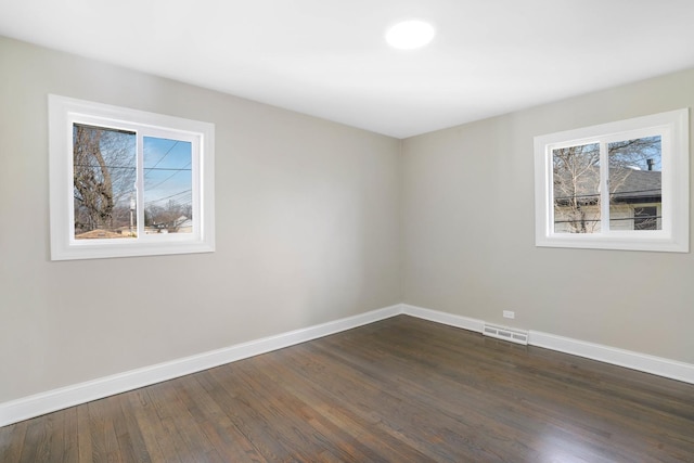 spare room featuring dark wood-style floors, visible vents, and baseboards