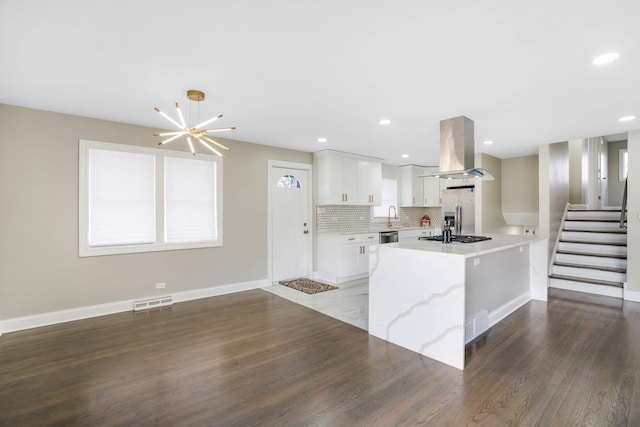 kitchen featuring wood finished floors, island exhaust hood, stainless steel appliances, white cabinetry, and tasteful backsplash