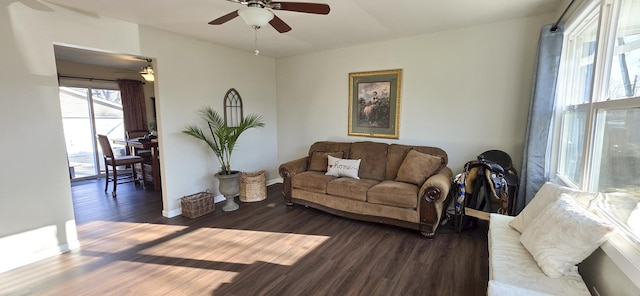 living area with dark wood-type flooring, a ceiling fan, and baseboards