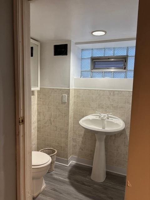 bathroom with toilet, tile walls, and wood finished floors