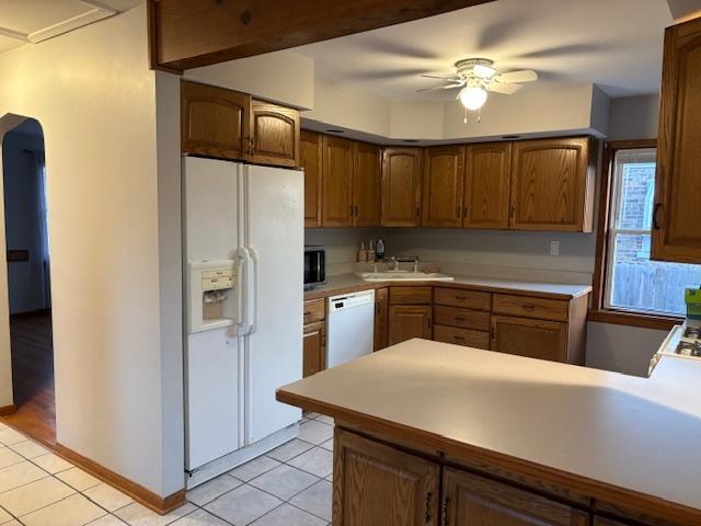 kitchen with white appliances, a peninsula, light tile patterned flooring, ceiling fan, and light countertops