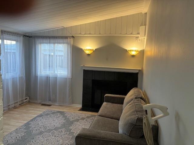 living room with wood finished floors, visible vents, a baseboard radiator, a fireplace, and vaulted ceiling