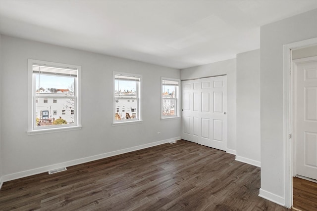 unfurnished bedroom featuring dark wood finished floors, visible vents, a closet, and baseboards