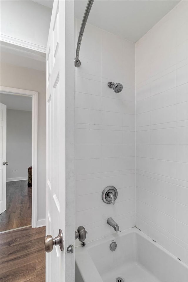 bathroom with baseboards, wood finished floors, and washtub / shower combination