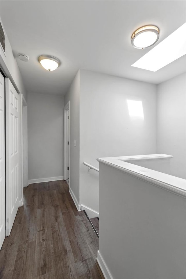 hall featuring dark wood-style floors, an upstairs landing, baseboards, and a skylight