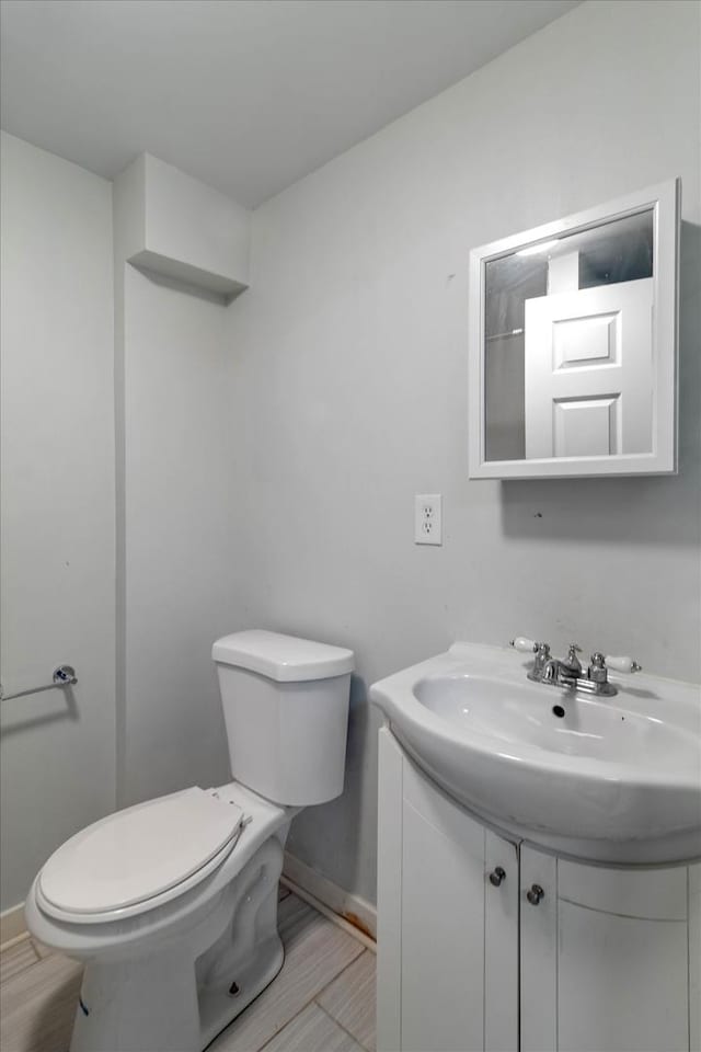 bathroom featuring toilet, vanity, baseboards, and wood finished floors