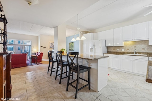 kitchen featuring tasteful backsplash, a breakfast bar area, dark stone countertops, white fridge with ice dispenser, and a sink