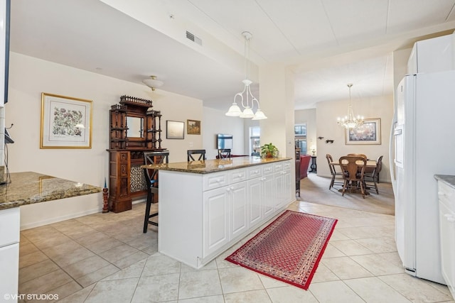 kitchen featuring visible vents, a chandelier, a kitchen breakfast bar, freestanding refrigerator, and white cabinetry