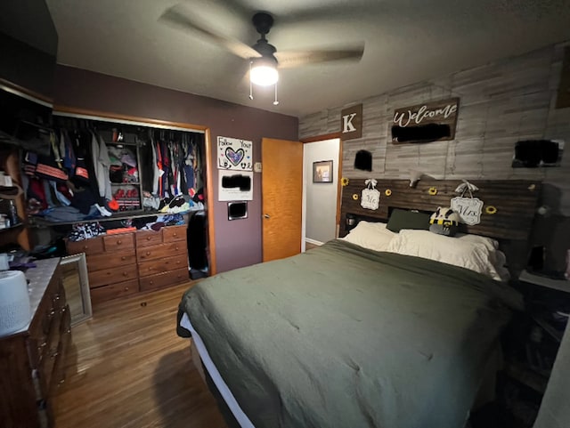 bedroom featuring a closet, wood walls, ceiling fan, and wood finished floors