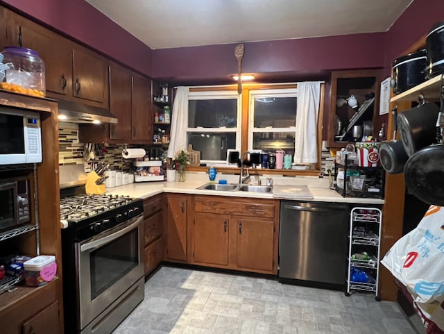 kitchen featuring under cabinet range hood, light countertops, dishwashing machine, gas stove, and a sink