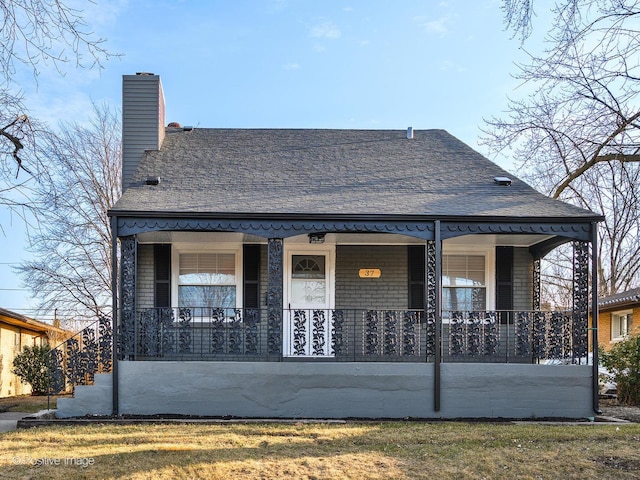 view of front facade featuring a shingled roof, covered porch, and a chimney