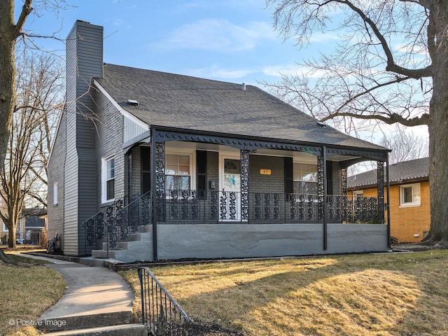 view of front of home featuring a chimney, roof with shingles, covered porch, and a front lawn