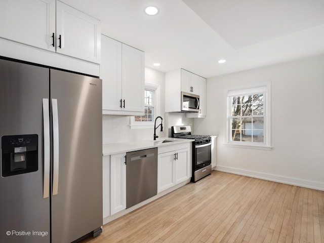 kitchen featuring a sink, light countertops, white cabinets, appliances with stainless steel finishes, and light wood-type flooring