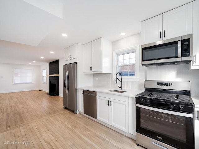 kitchen featuring light wood-type flooring, a sink, white cabinetry, stainless steel appliances, and light countertops