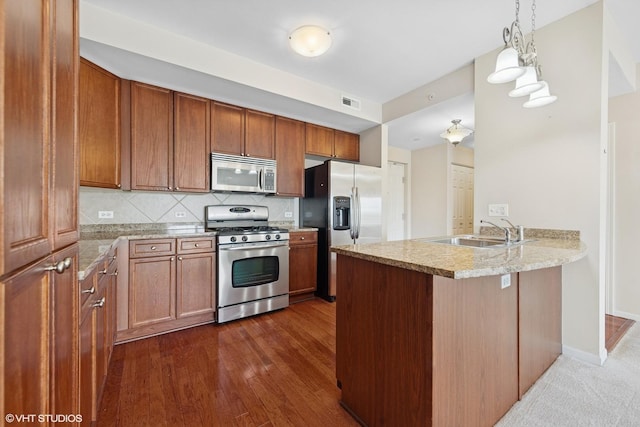 kitchen with tasteful backsplash, brown cabinets, appliances with stainless steel finishes, a peninsula, and a sink