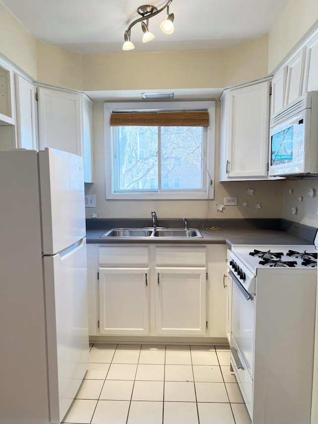 kitchen with a sink, dark countertops, white appliances, white cabinets, and light tile patterned floors