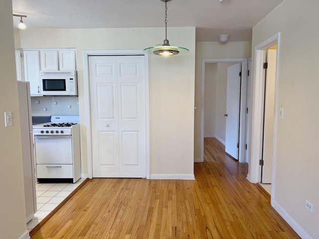 kitchen featuring decorative light fixtures, white appliances, light wood-style floors, white cabinets, and baseboards